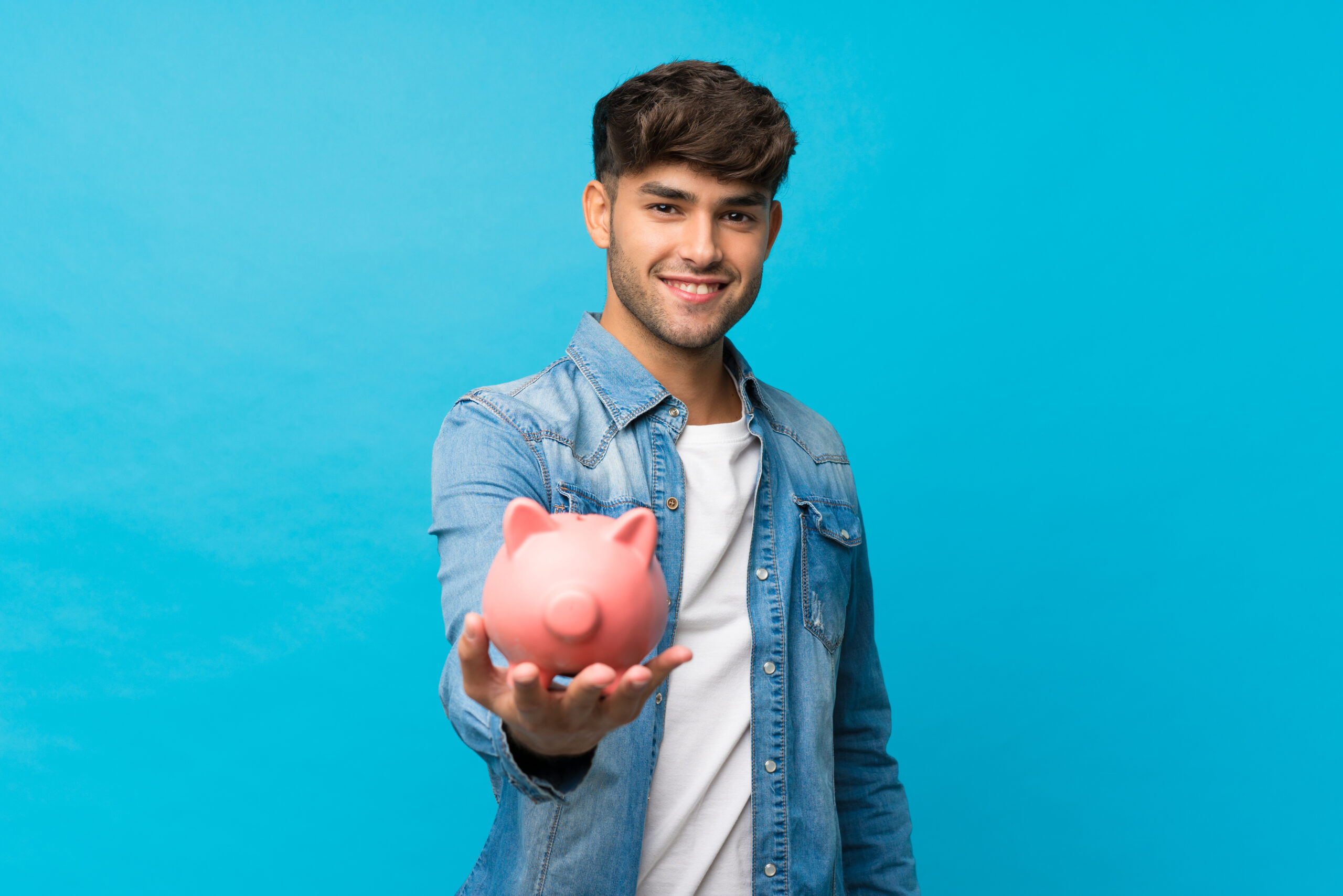 Young handsome man over isolated blue background holding a big piggybank